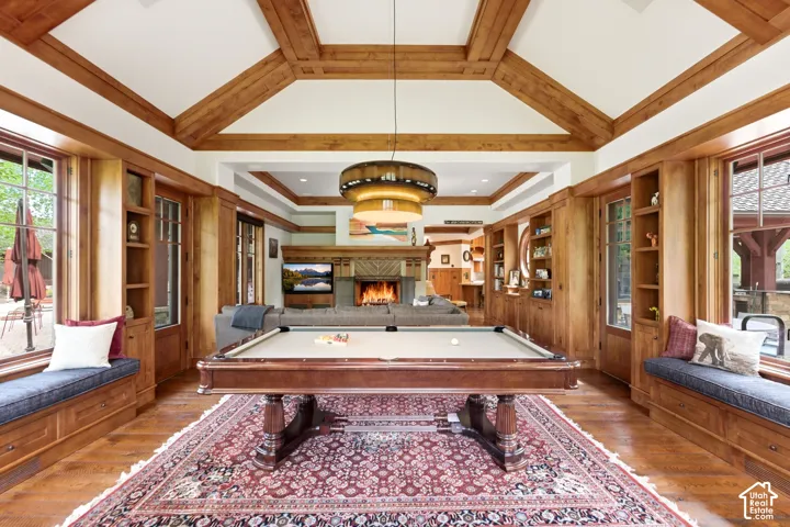 Vaulted ceiling with exposed wood beams, built-in window seating, extensive wood paneling, integrated shelving, and wood-finish flooring