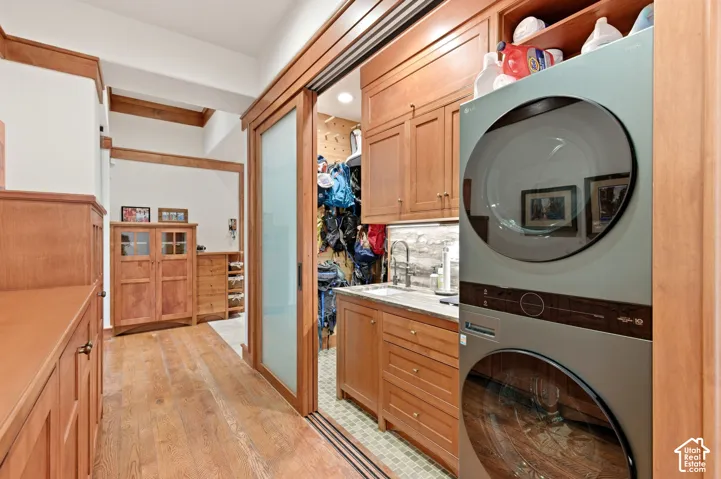 Wood-finish flooring, built-in cabinetry, exposed wood beams, sliding frosted glass door, and stacked laundry appliances