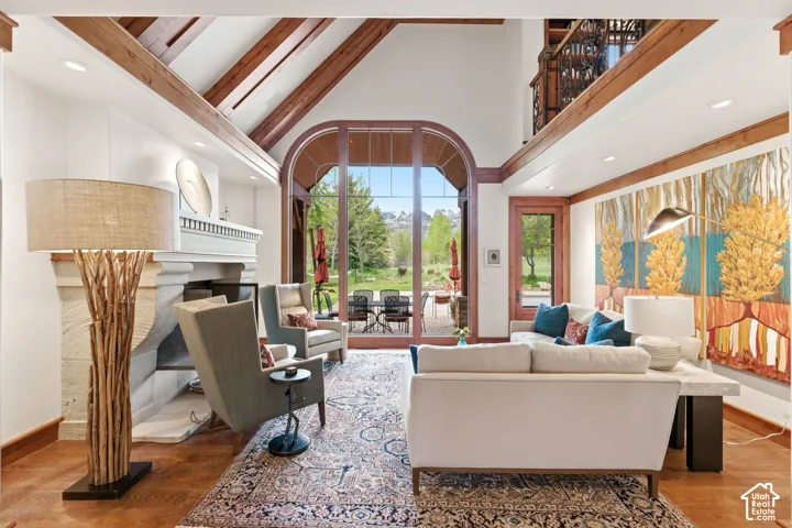 Vaulted ceiling with exposed wood beams, stone fireplace, arched glass door, and hardwood flooring
