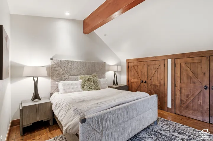 Wood-finish flooring, exposed wood beam, two wood-finish barn-style doors, recessed lighting, and a sloped ceiling