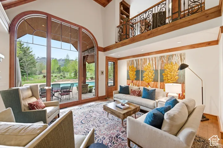 Vaulted ceilings with exposed wood beams, a second-story balcony with wrought iron railing, expansive arched windows, wood-finish flooring, and a built-in bookshelf