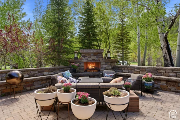 Paver patio with a stone-clad outdoor fireplace, built-in stone seating, and tiered stone retaining walls