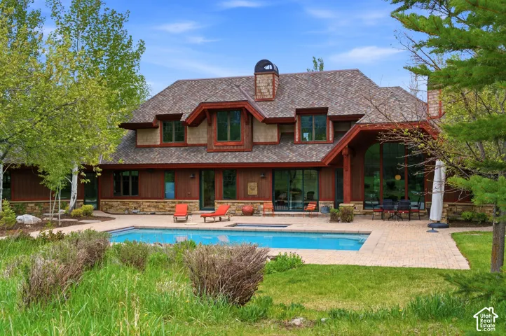 Craftsman-style exterior with stone and wood siding, featuring a substantial outdoor pool, an expansive patio, and large windows