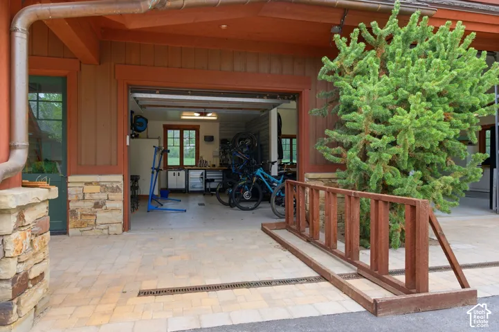 Covered patio with rustic wood railing and stone veneer accents, opening to a spacious garage with overhead door