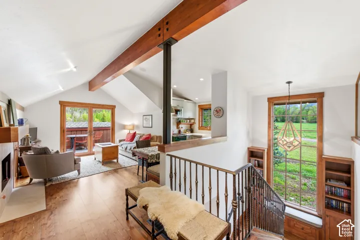 Vaulted ceiling with exposed wood beams, wood-finish flooring, built-in fireplace, sliding glass doors, and a large picture window with built-in shelving