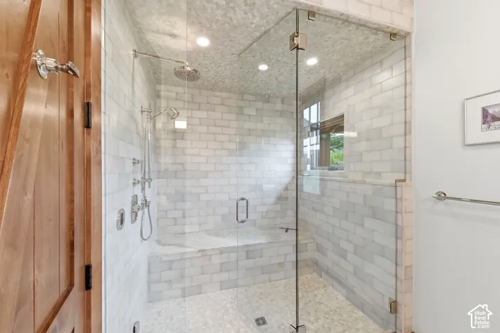 Glass-enclosed shower with subway tile walls, a built-in bench, dual shower heads, and pebble-tile flooring