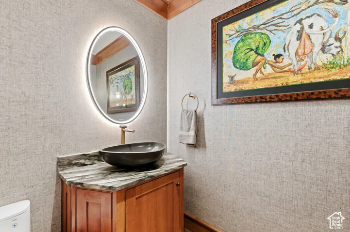 Vanity with stone countertop, vessel sink, and an illuminated oval mirror