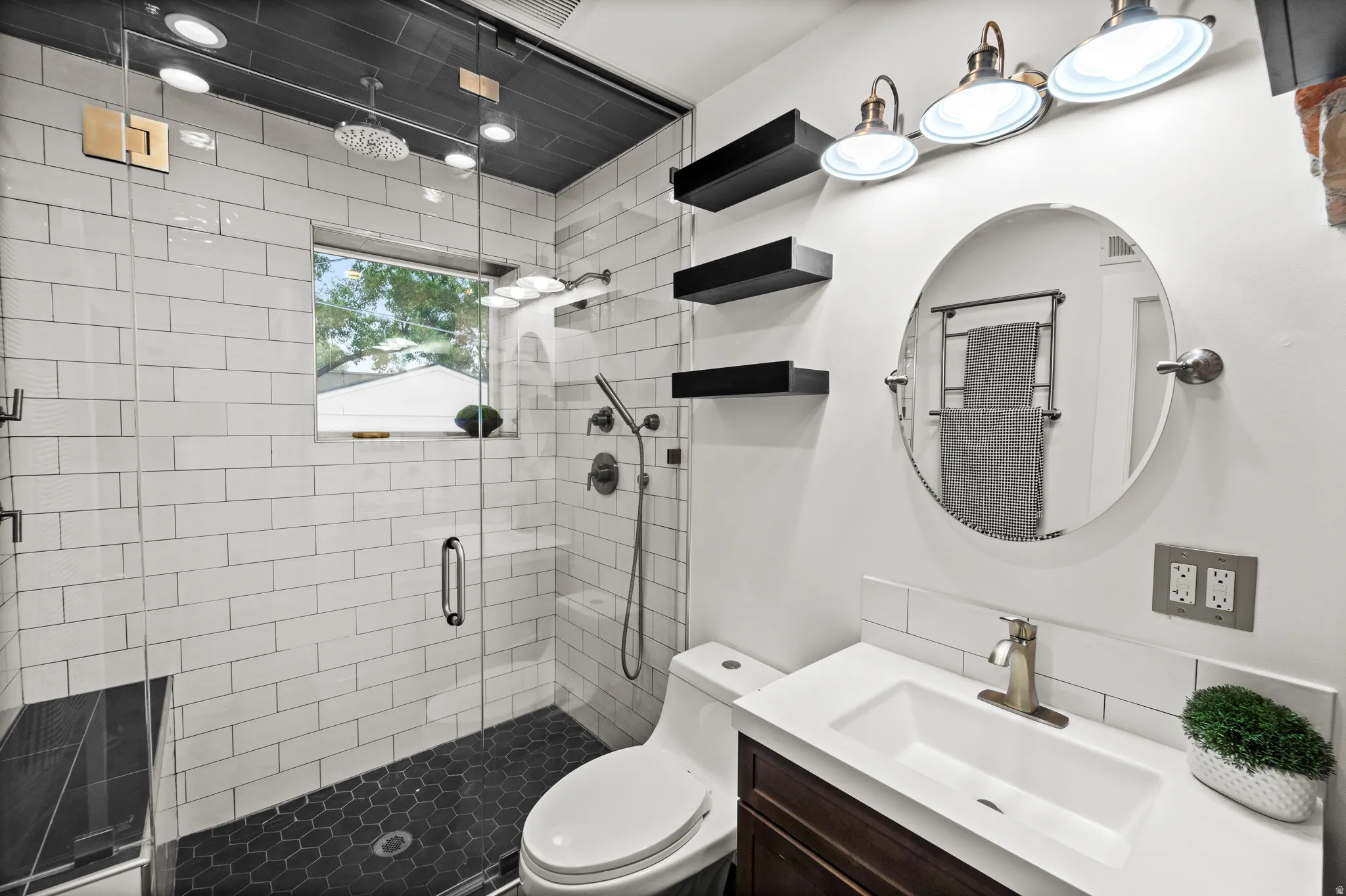 Contemporary bathroom featuring a spacious glass-enclosed shower with white subway tile walls and dark hexagonal floor tile