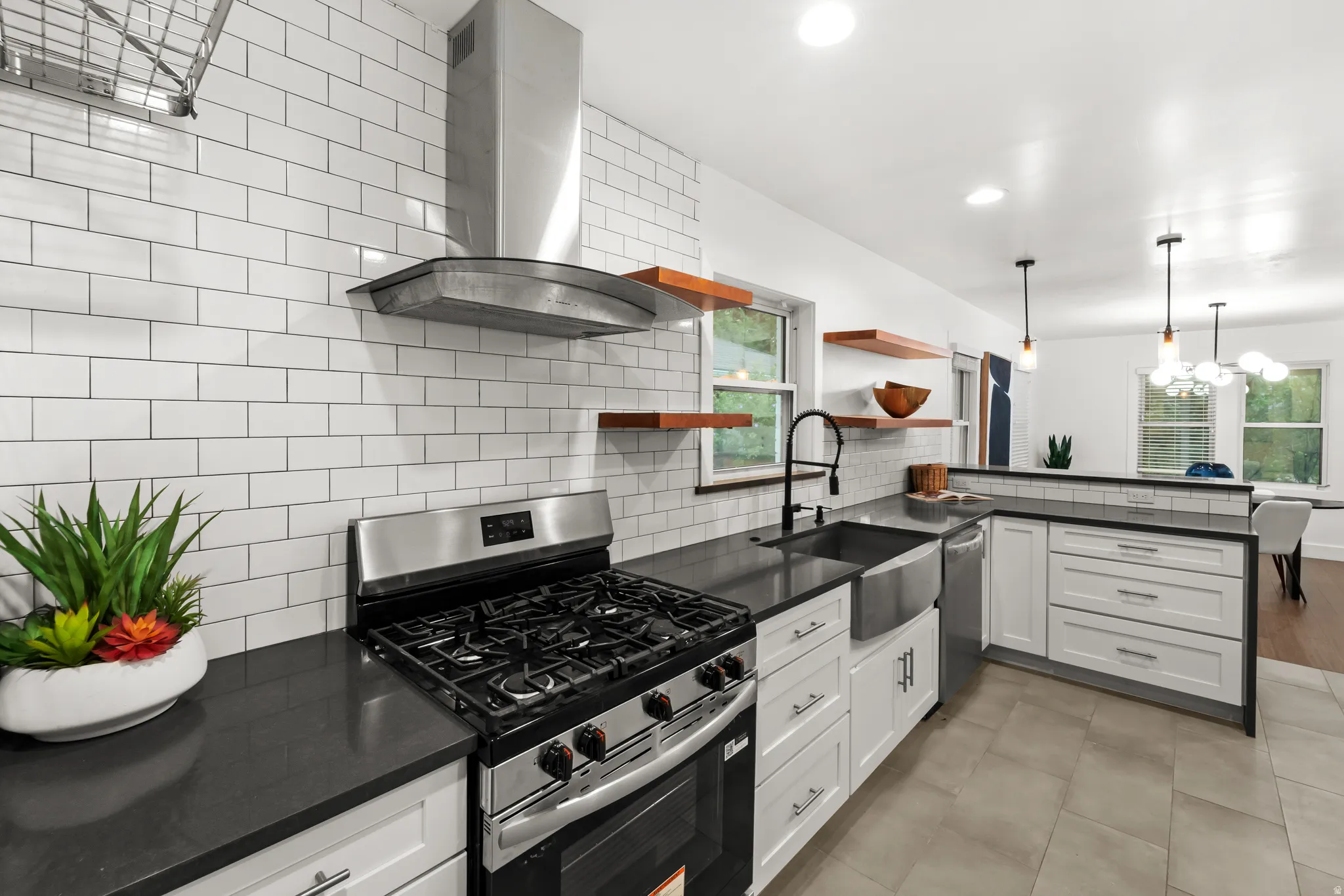 Modern kitchen featuring white shaker cabinetry, dark countertops, a stainless steel range with matching hood, and a farmhouse sink with a gooseneck faucet