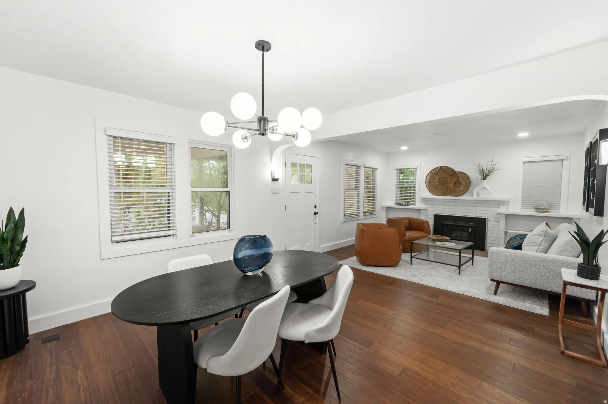 Spacious living area featuring wood-finish flooring, a modern chandelier, and a white-tiled fireplace with built-in shelving