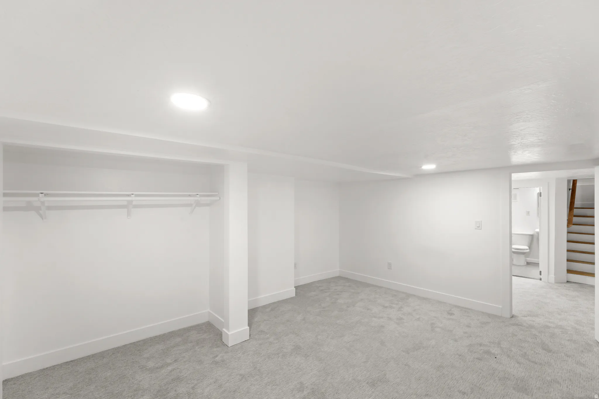 Spacious room with new gray carpeting, crisp white walls, and recessed lighting