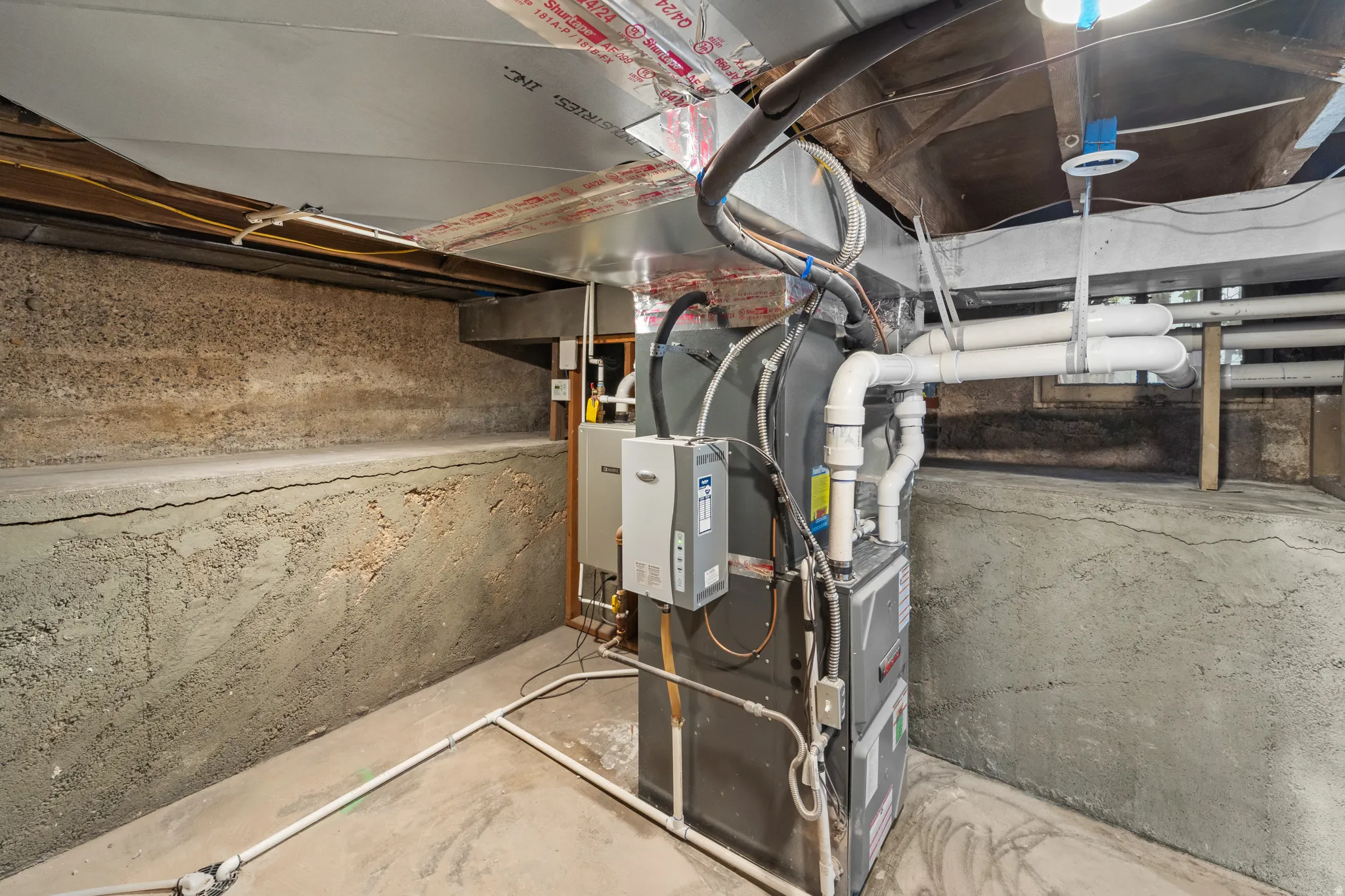 Utility area featuring a furnace system and water heater, exposed concrete walls, and overhead ductwork