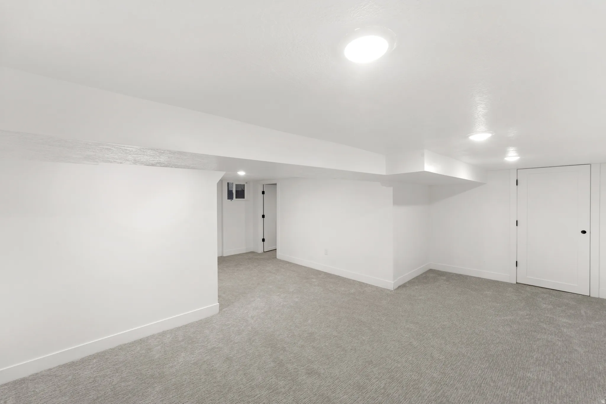 Spacious room featuring light gray carpeting, white painted walls, recessed lighting, and white baseboards