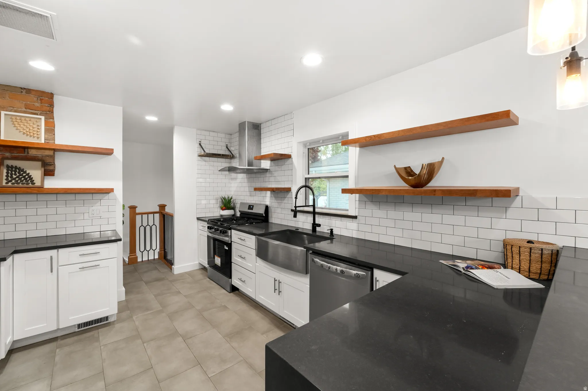 Contemporary kitchen featuring dark countertops, white subway tile backsplash, stainless steel appliances, a farmhouse sink with a black faucet, and open wood shelving