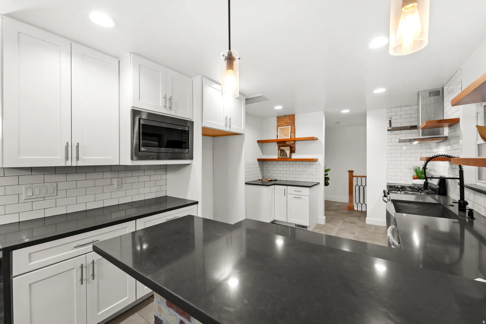 Kitchen featuring a large central island with dark countertops, white shaker cabinetry, subway tile backsplash, and recessed lighting