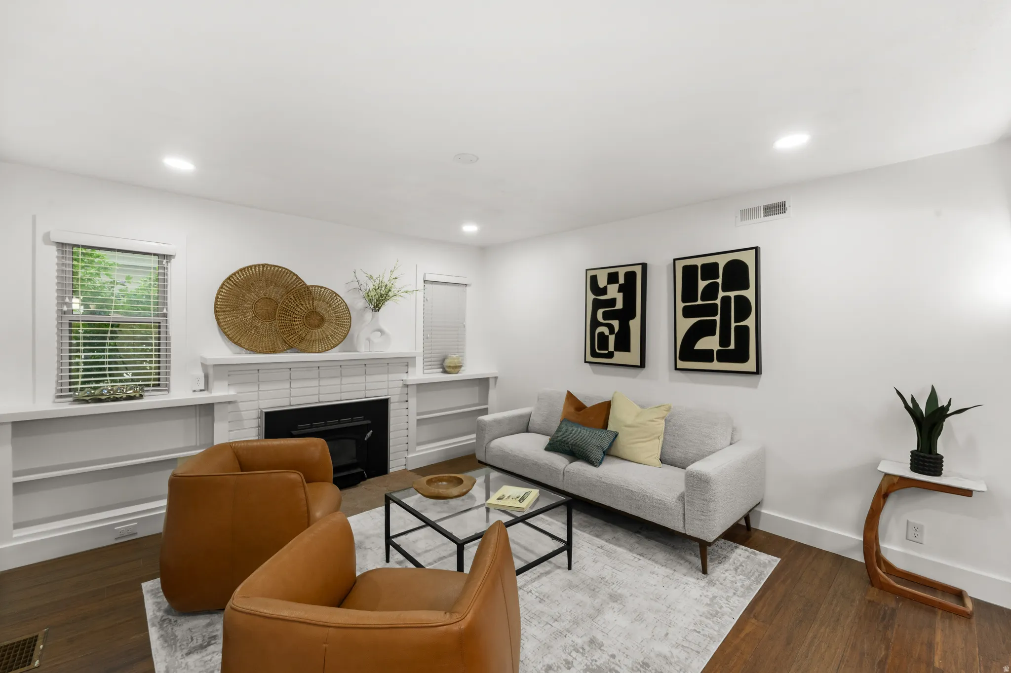 Living area featuring wood-finish flooring, a white brick fireplace with a black insert, recessed lighting, and built-in shelving