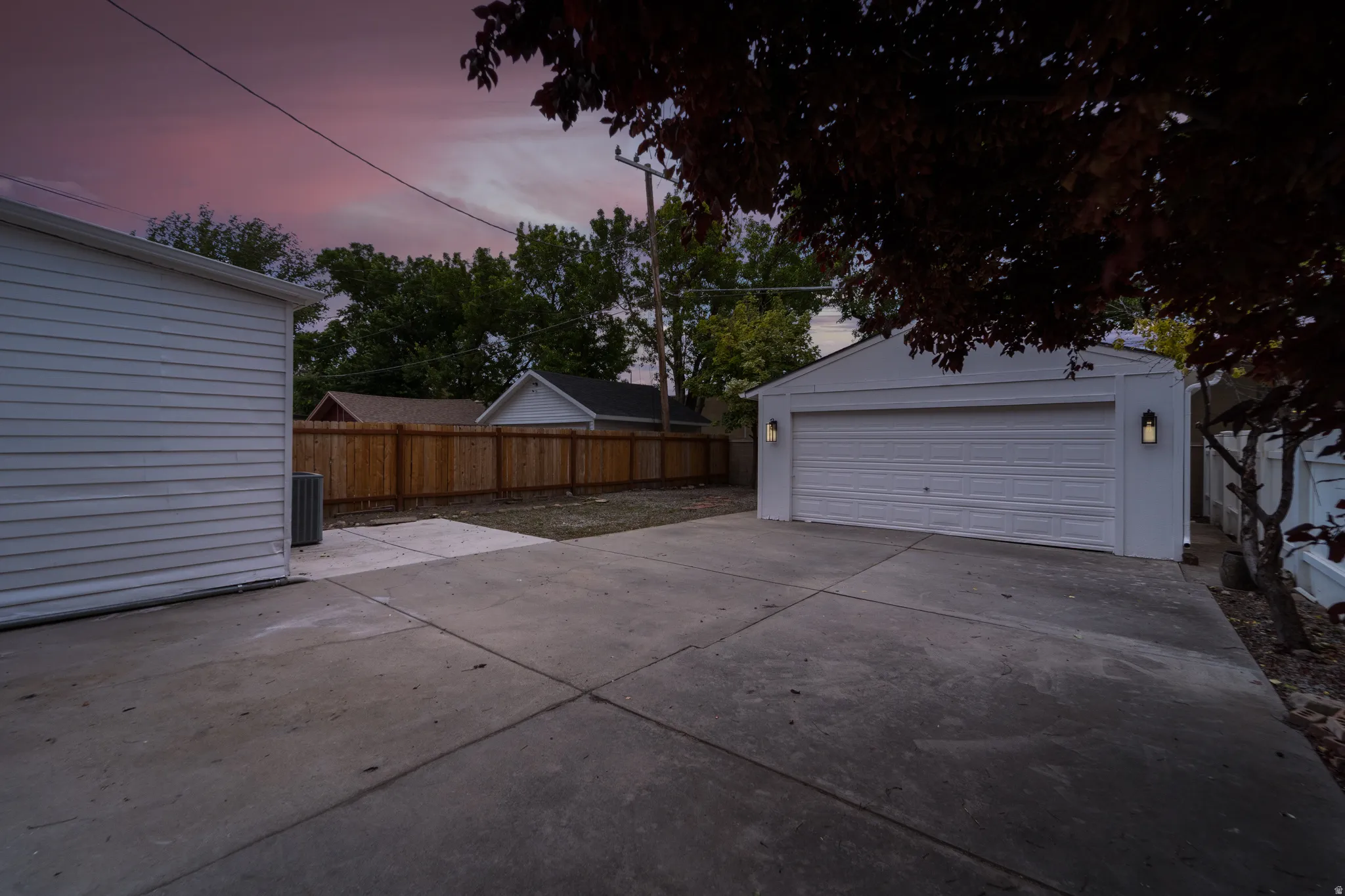 Detached two-car garage with modern outdoor sconces, concrete driveway, and a wood privacy fence