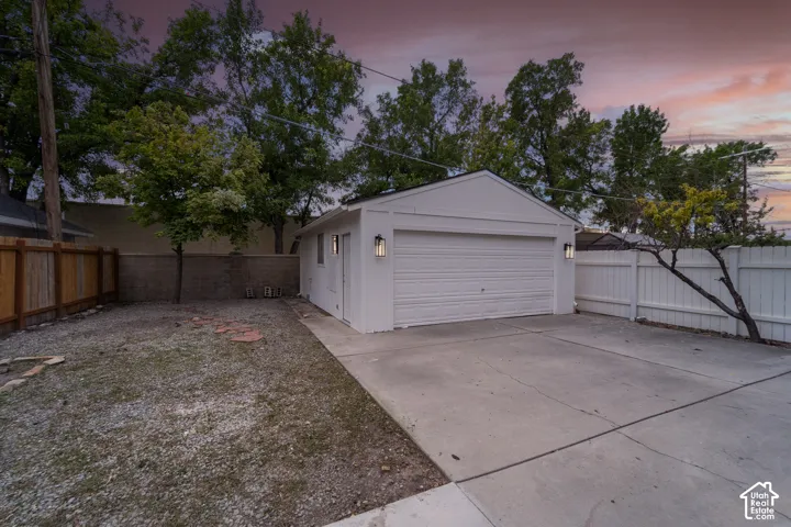Detached white garage featuring a two-car garage door, two exterior wall sconces, and a side entrance