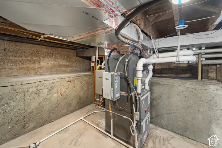 Utility area featuring a furnace system and water heater, exposed concrete walls, and overhead ductwork