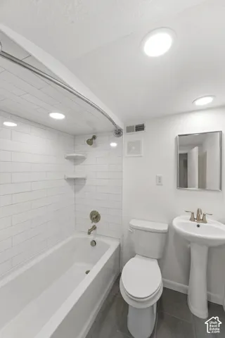 Bathroom featuring a white bathtub with subway tile surround, pedestal sink, toilet, and gray tile flooring