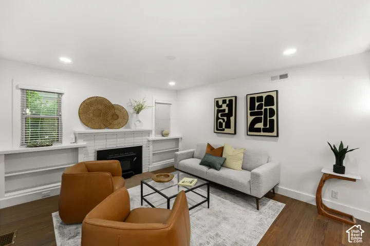 Living area featuring wood-finish flooring, a white brick fireplace with a black insert, recessed lighting, and built-in shelving