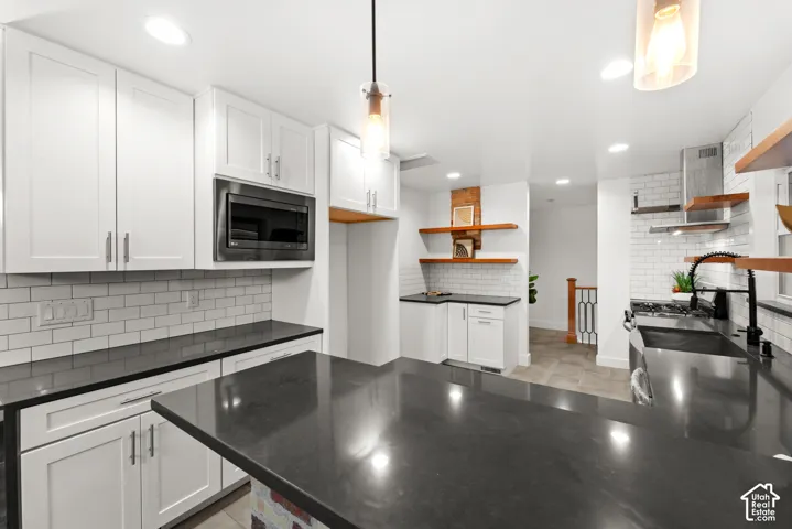 Kitchen featuring a large central island with dark countertops, white shaker cabinetry, subway tile backsplash, and recessed lighting