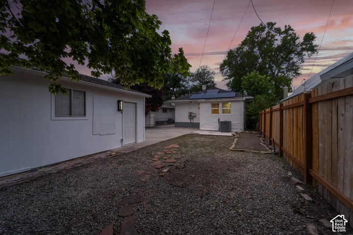 Expansive gravel yard featuring a wood privacy fence, concrete patio, and a separate white accessory structure with solar panels