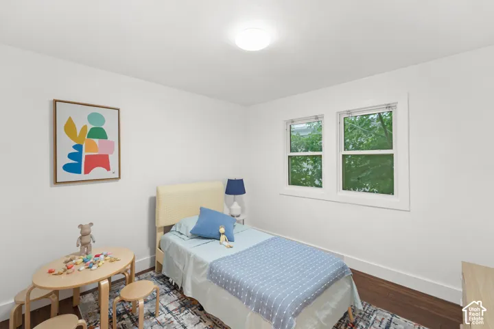 Bedroom featuring wood-finish flooring, two large windows, white trim, and a flush-mount ceiling light