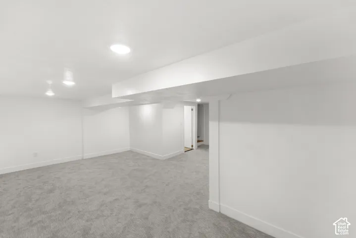Spacious room featuring light gray carpet, recessed lighting, white walls, and a visible doorway leading to a staircase