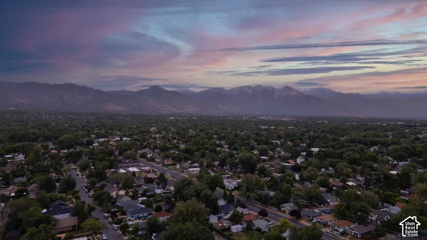 Expansive neighborhood setting featuring a dense canopy of mature trees, residential properties with varied architectural styles, and distant mountains with snow-capped peaks
