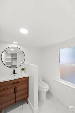 Primary full bathroom featuring a wood-finish vanity with integrated sink, a circular black-framed mirror, recessed lighting, and white marble-look floor tiles