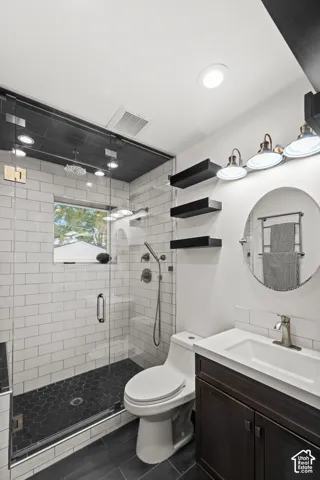 Contemporary bathroom featuring a dark wood-finish vanity with a white integrated sink, a framed glass shower enclosure with white subway tile walls, a dark hexagonal tile shower floor, and dark wood-finish flooring