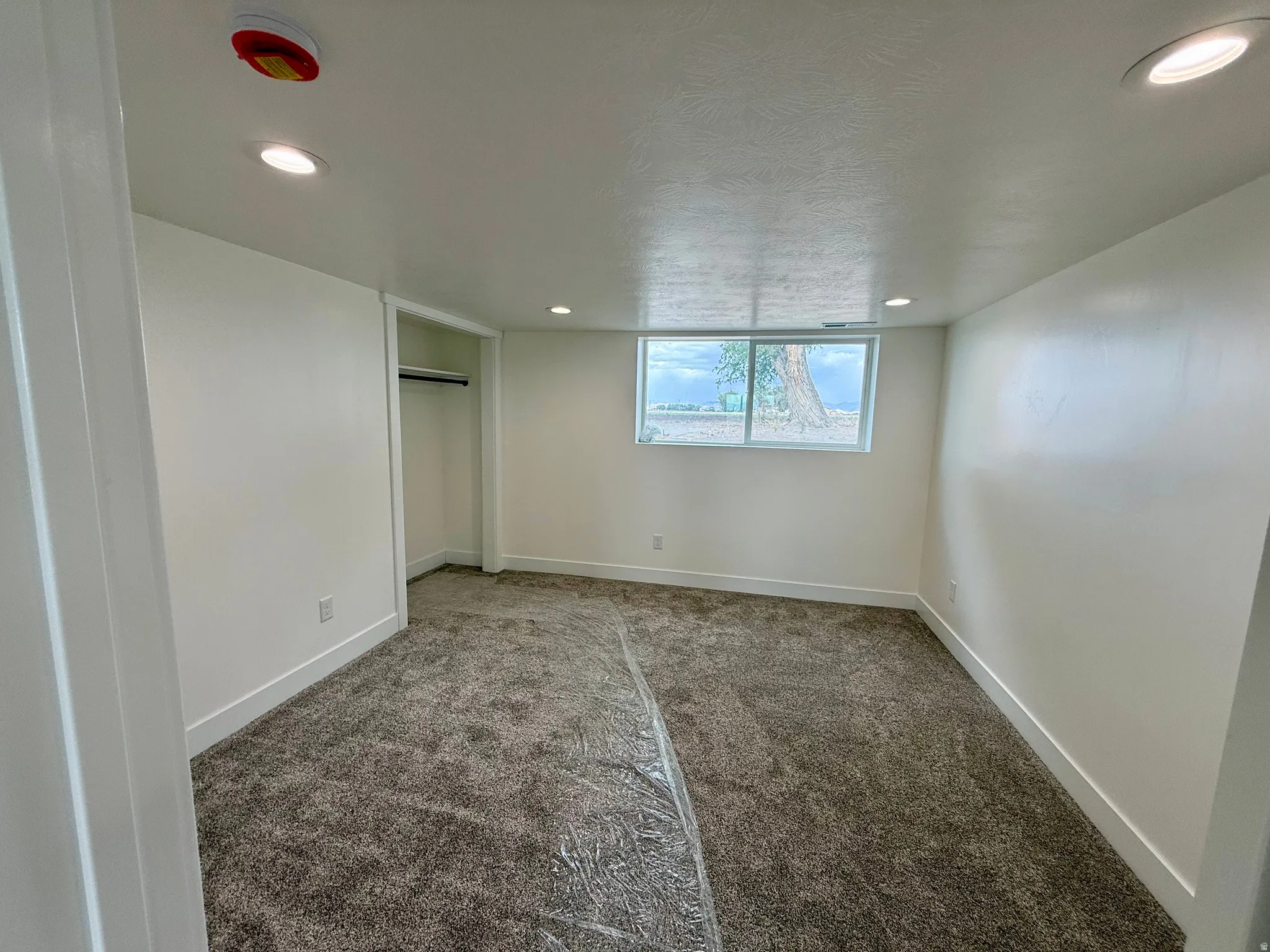Spacious room featuring neutral carpeting, white walls, recessed lighting, and a window with a natural backdrop