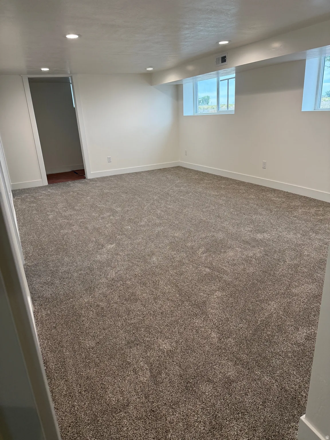 Spacious room featuring new carpeting, recessed lighting, white walls, and two egress windows