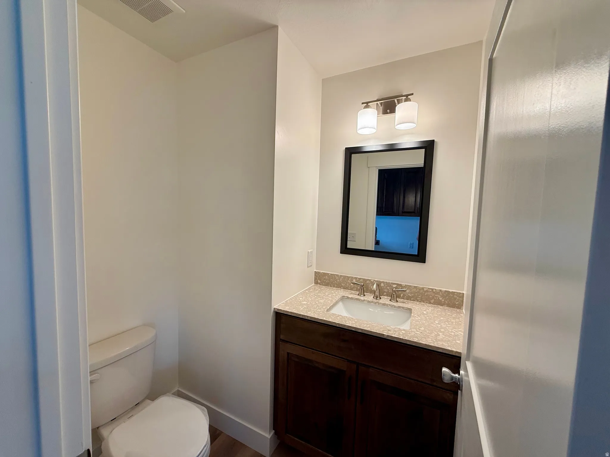 Bathroom featuring a dark wood vanity with a light speckled countertop, undermount sink, and a framed mirror