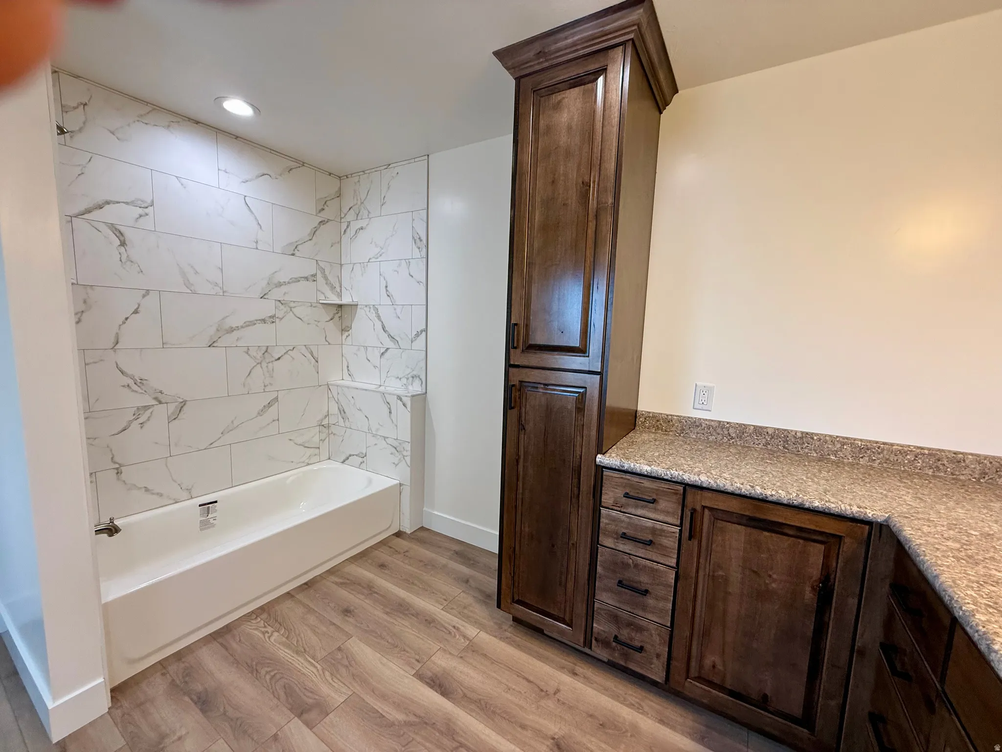 Bathroom featuring a white tub with marble-look tile surround and recessed lighting