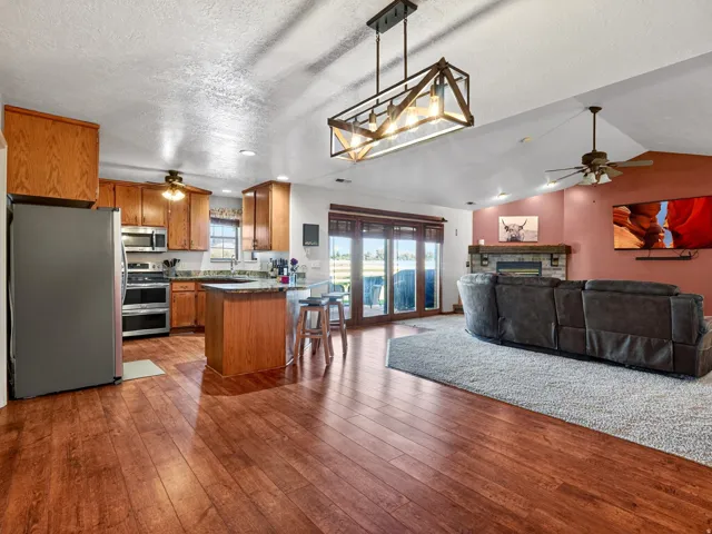 Open-concept living area featuring wood-finish flooring, a kitchen island with seating, stainless steel appliances, a stone-front fireplace with a wood mantle, and sliding glass doors