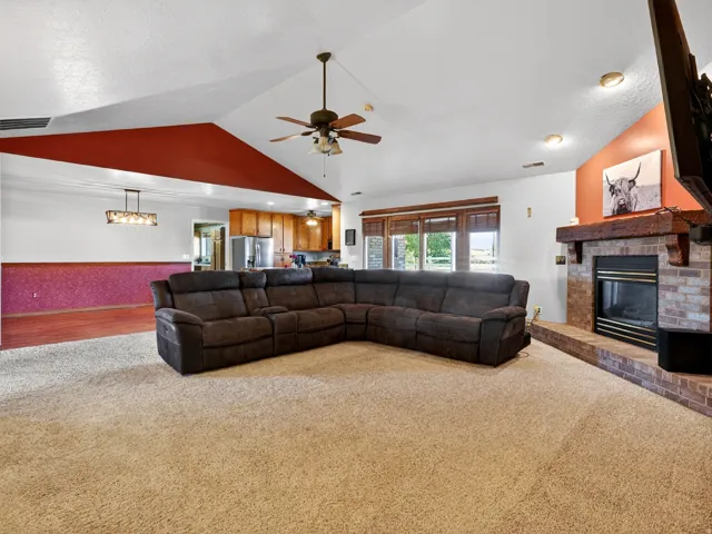 Open-concept living space featuring a vaulted ceiling and a brick fireplace with a wood mantel