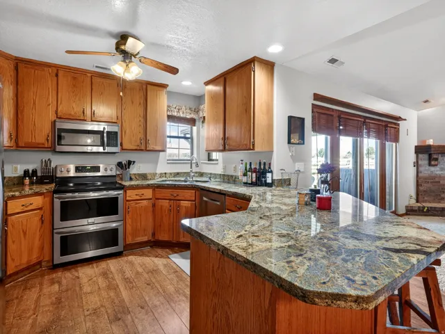 Kitchen featuring wood-finish flooring, oak cabinetry, stainless steel appliances, and granite countertops with a breakfast bar