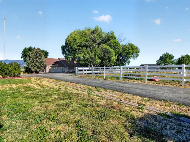 Paved driveway leading to a residence with a two-car garage, surrounded by mature trees and a white vinyl fence