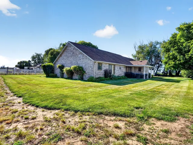 Expansive green lawn surrounds the property, featuring a brick exterior, a covered patio, and established trees