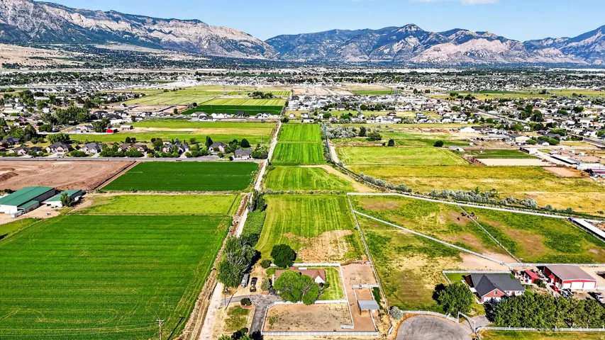 Expansive agricultural land featuring cultivated fields and scattered residential properties, set against a mountainous backdrop