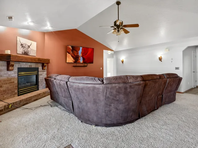 Living area featuring a vaulted ceiling and brick fireplace with a wood-beam mantel
