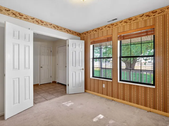 Carpeted room featuring two paneled doors, two windows with blinds, and striped wallpaper with a decorative border
