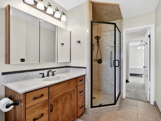 Bathroom featuring a glass-enclosed shower with tile surround, a vanity with a light-toned countertop, a rectangular undermount sink, and dark bronze fixtures
