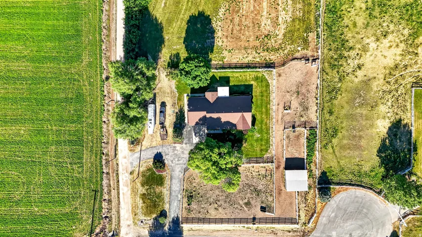 Expansive acreage featuring a central residence with a brown shingle roof, paved driveway, mature trees, and a detached outbuilding
