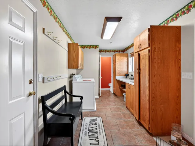 Spacious utility room featuring tile flooring, extensive wood-finish cabinetry, a utility sink with white countertop, and a bright overhead light fixture
