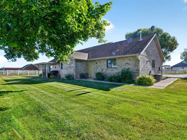 Expansive rear yard featuring a manicured lawn, mature trees, and a brick exterior with a covered patio