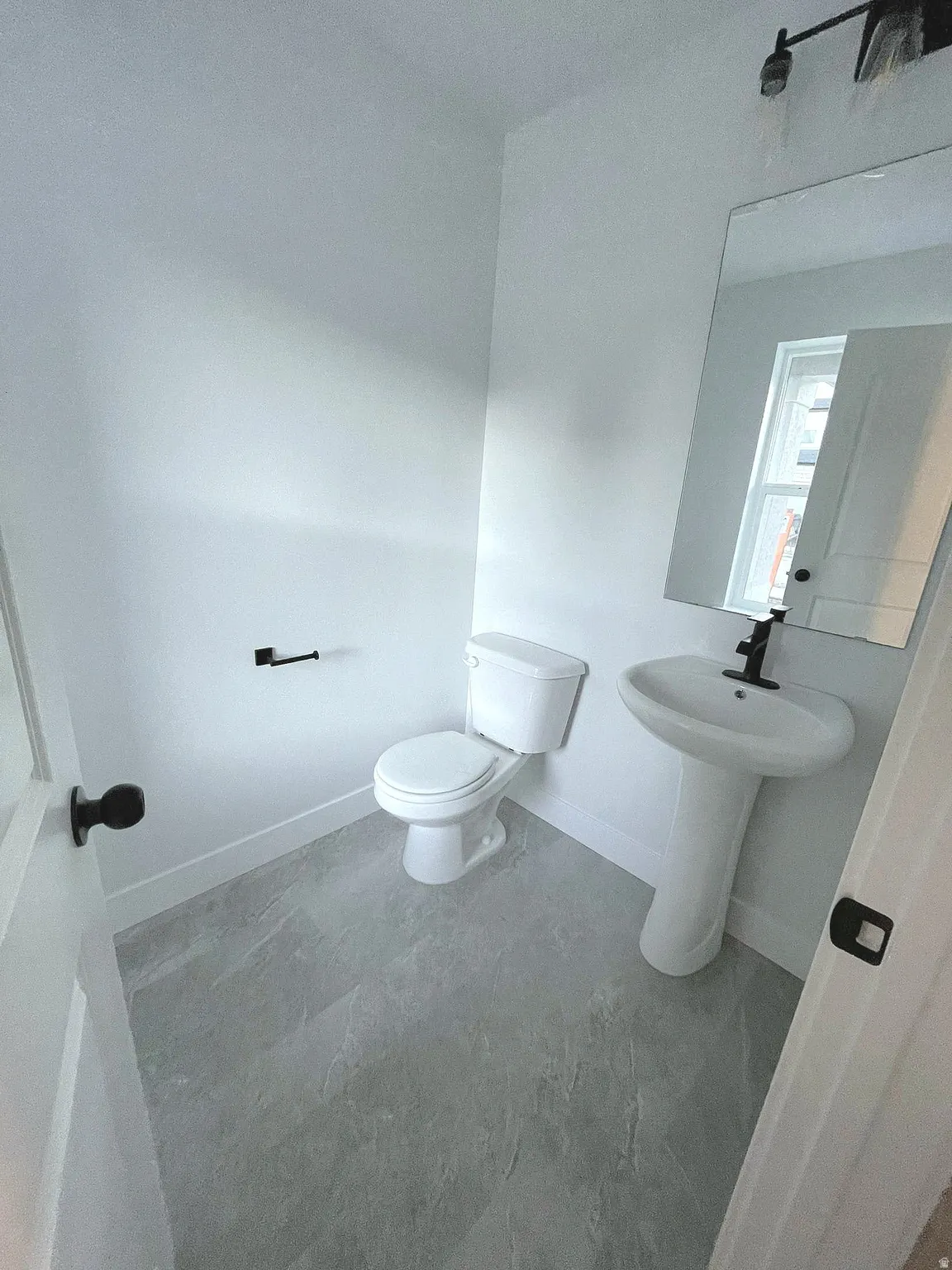 Pedestal sink with a matte black faucet, white toilet, and large rectangular wall mirror