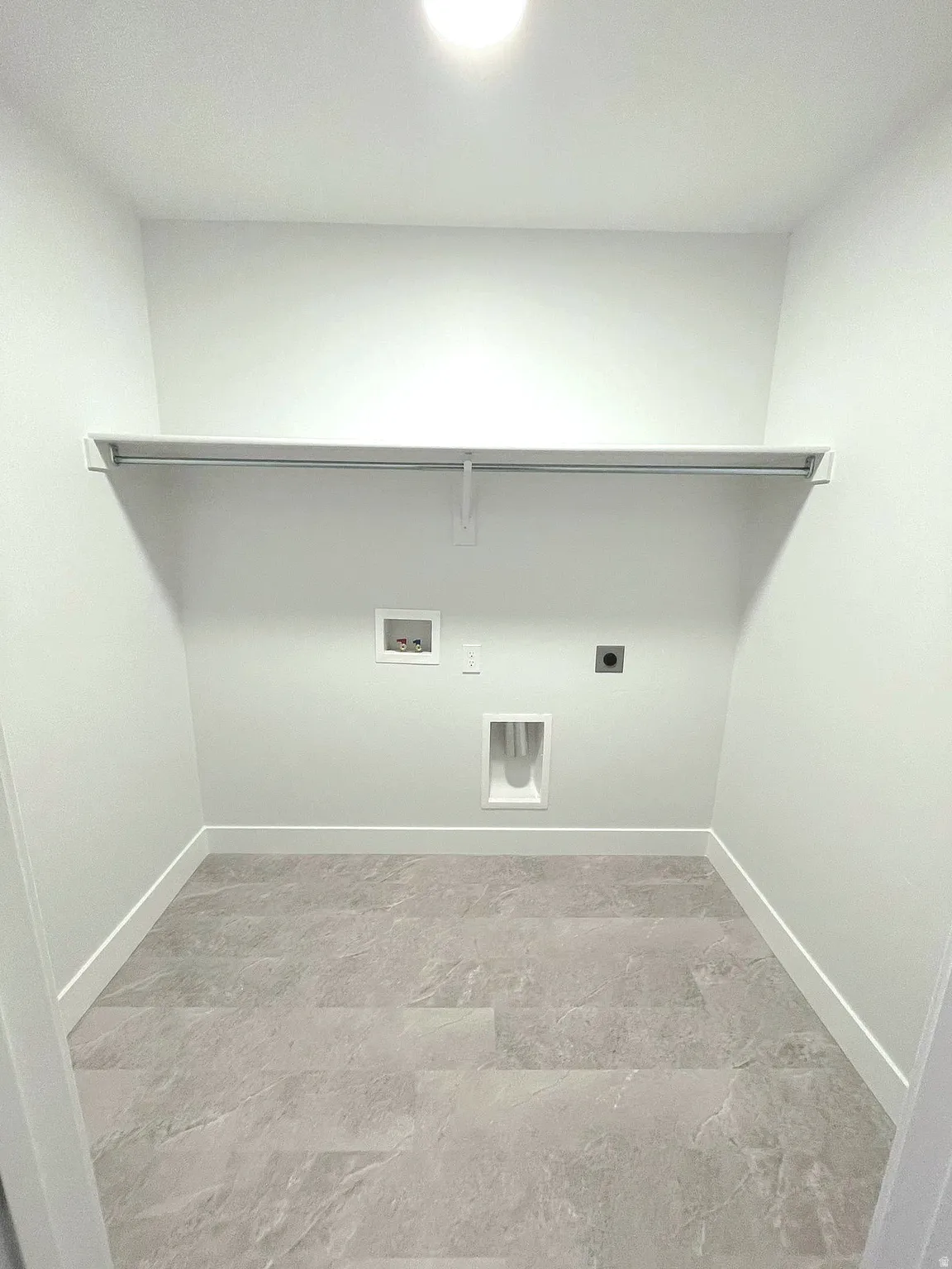 Dedicated utility space featuring light-toned flooring, white walls, and a built-in shelf with hanging rod